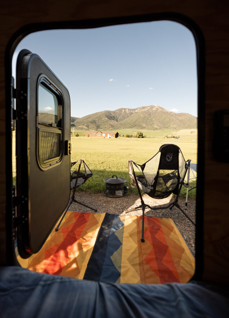 view of our campsite through our teardrop door. The campsite overlooks an open field with mountains nearby.